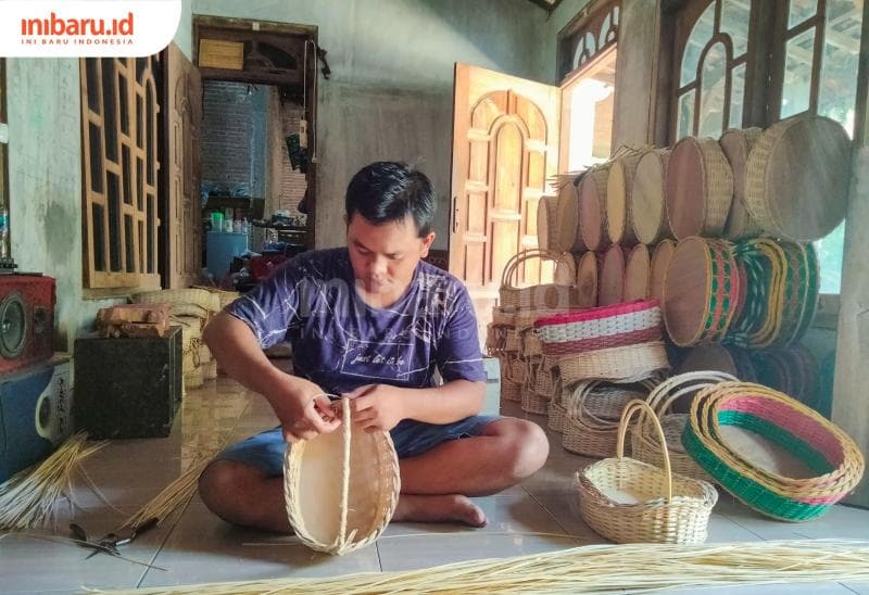 Arif tengah melilit rotan membentuk lengkungan sebagai pegangan keranjang.